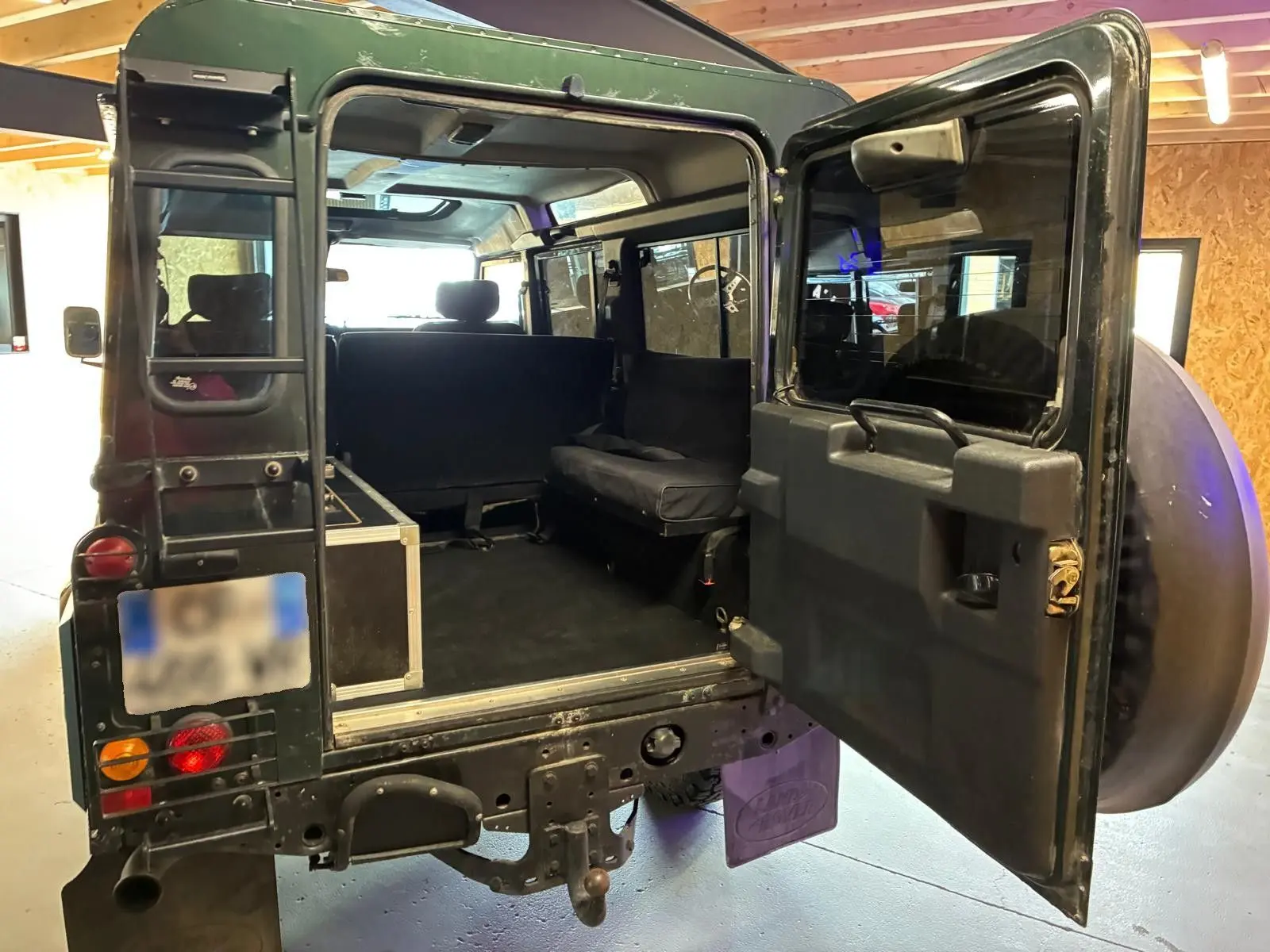 Vue arrière ouverte du Land Rover Defender 110 vert 2005, montrant l'intérieur spacieux et les sièges latéraux.