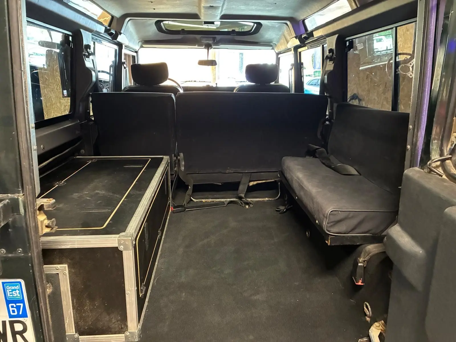 Vue intérieure arrière du Land Rover Defender 110 vert de 2005, montrant les sièges latéraux et un coffre noir.