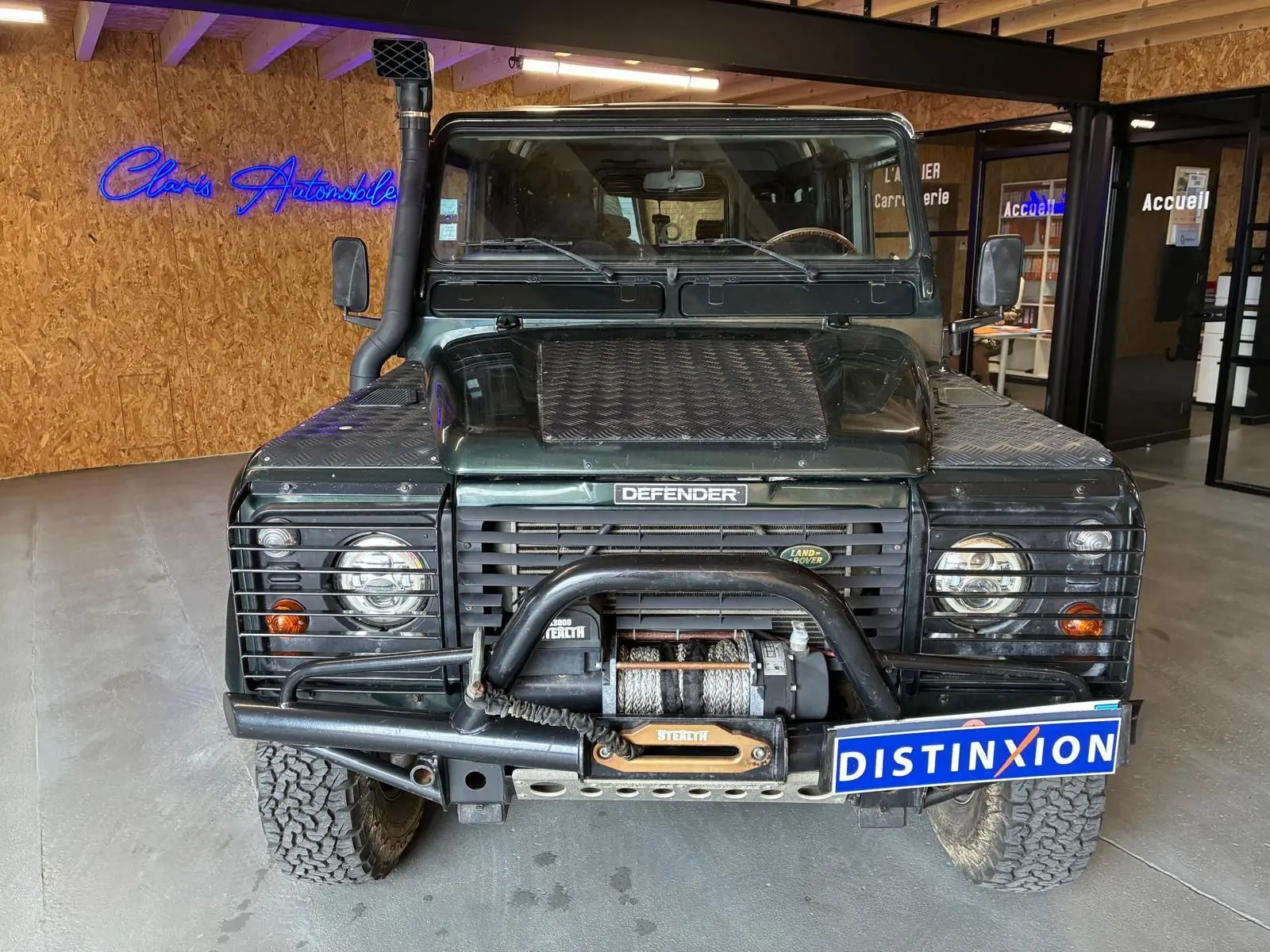 Vue frontale d’un Land Rover Defender 110 vert foncé de 2005 avec treuil et protections sur les phares.