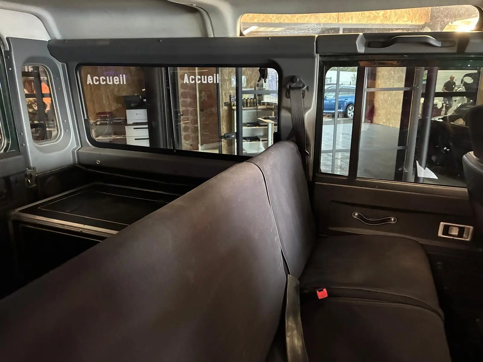 Vue intérieure côté droit du Land Rover Defender 110 vert de 2005, montrant la banquette arrière et les vitres coulissantes.