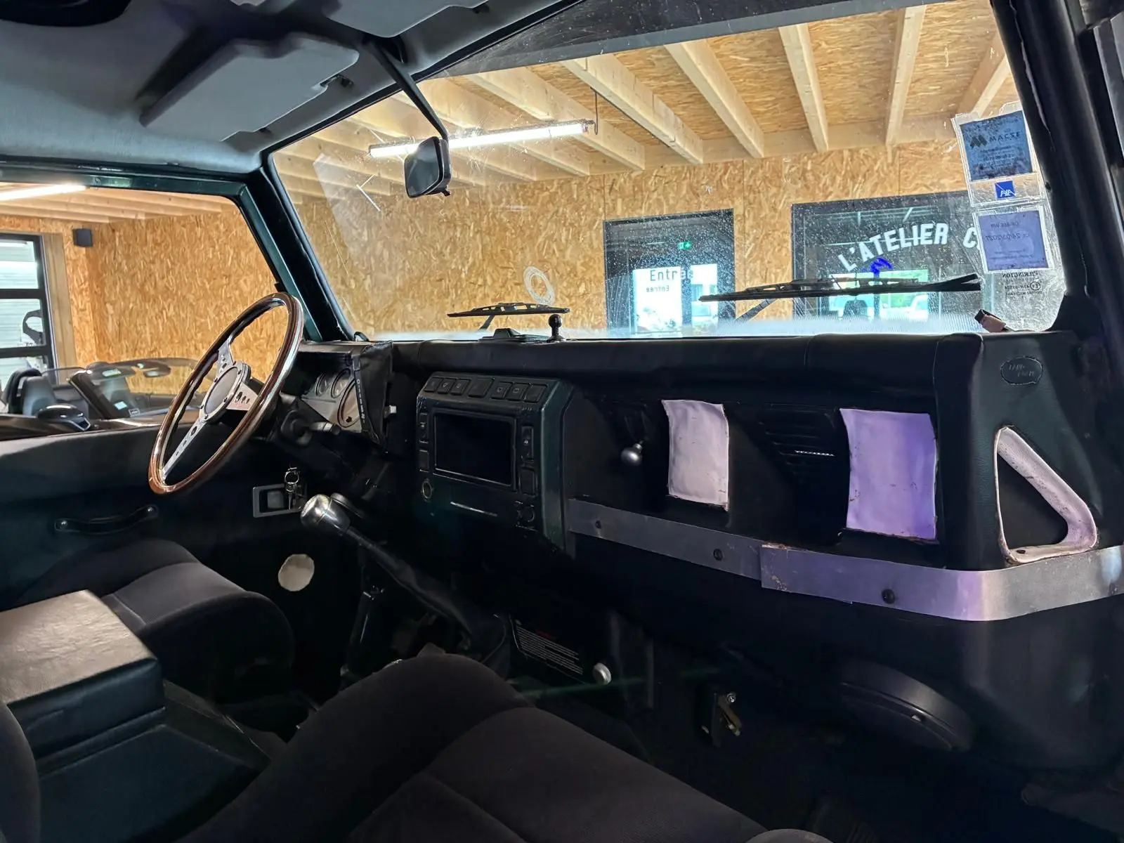 Vue intérieure côté conducteur du Land Rover Defender 110 2005, tableau de bord noir avec volant bois et levier de vitesse manuel.