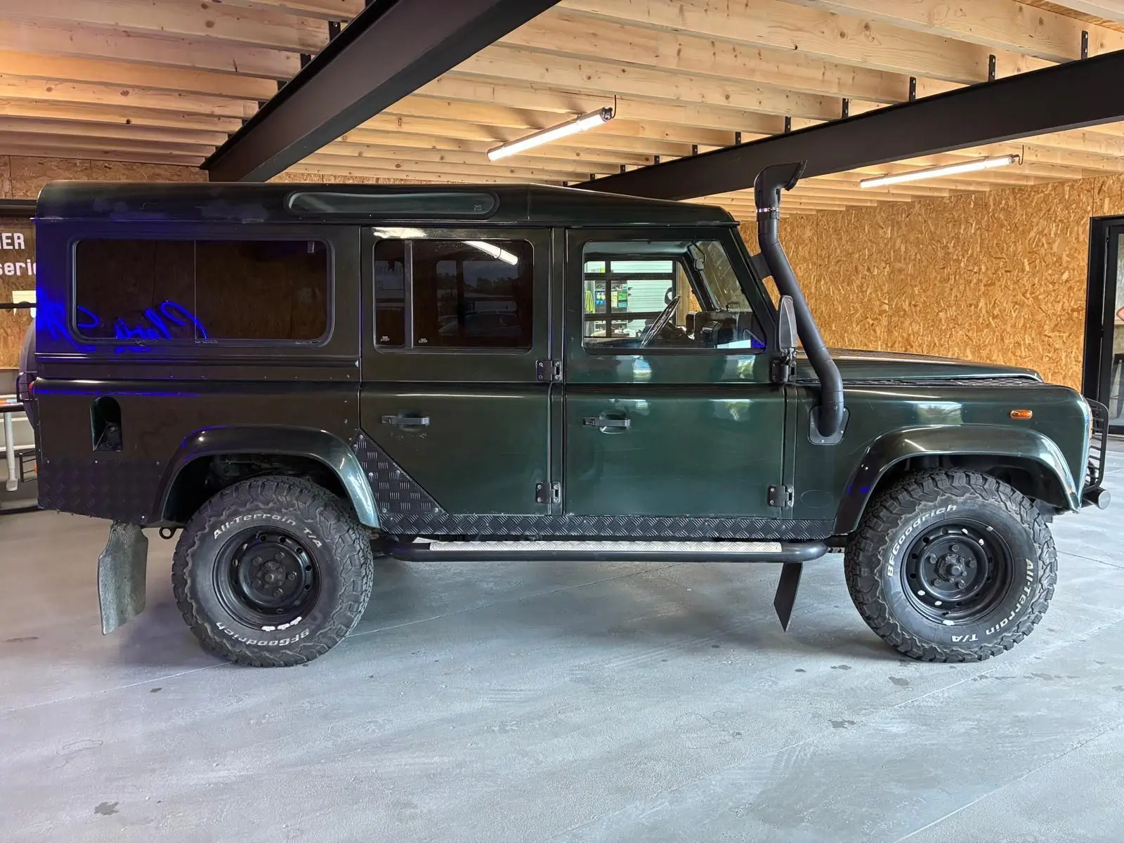 Vue de profil côté gauche d'un Land Rover Defender 110 vert 2005 avec pneus tout-terrain et snorkel noir.