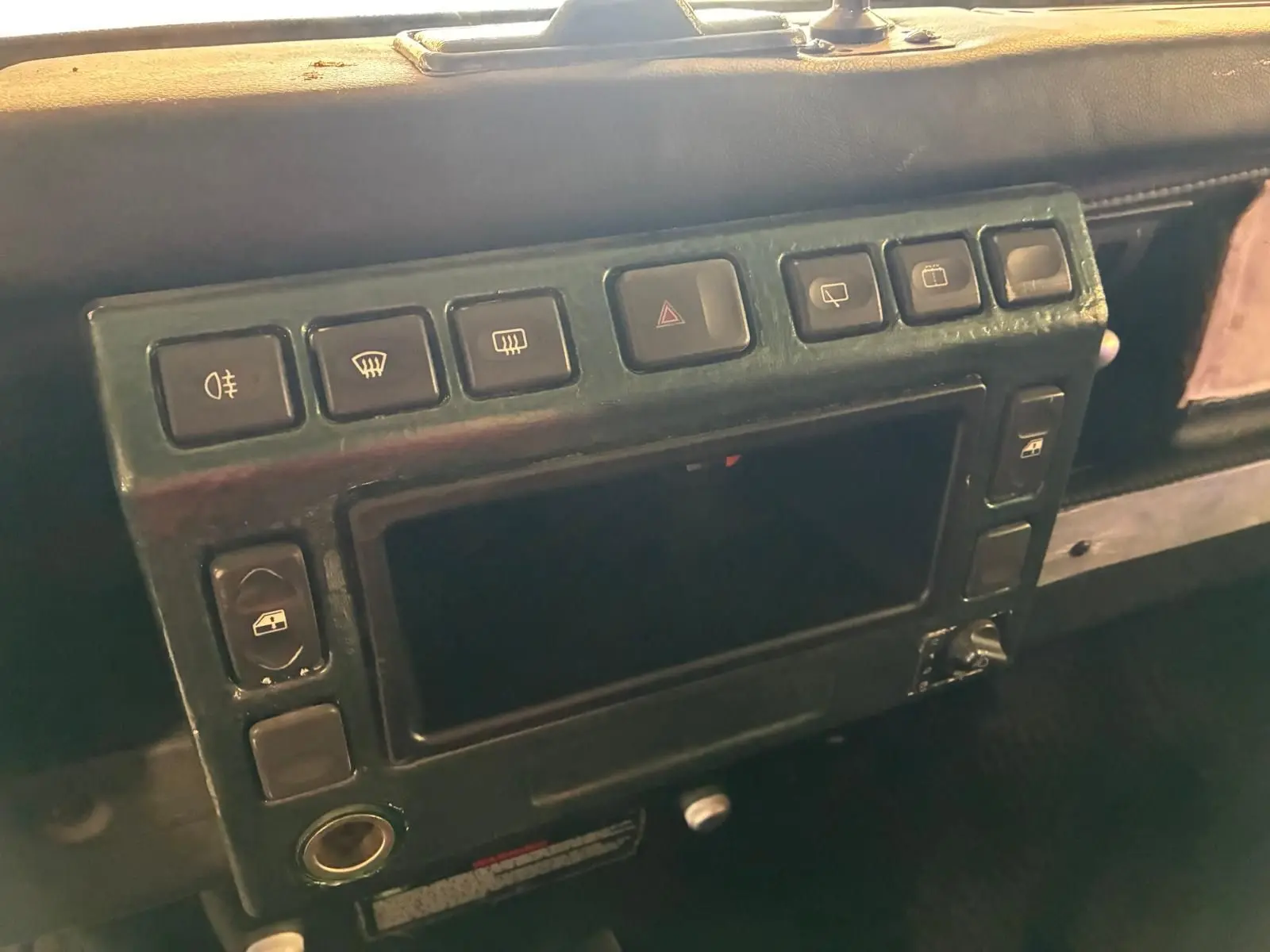 Détail du tableau de bord vert foncé du Land Rover Defender 110 2005, montrant les boutons de commande et la console centrale.