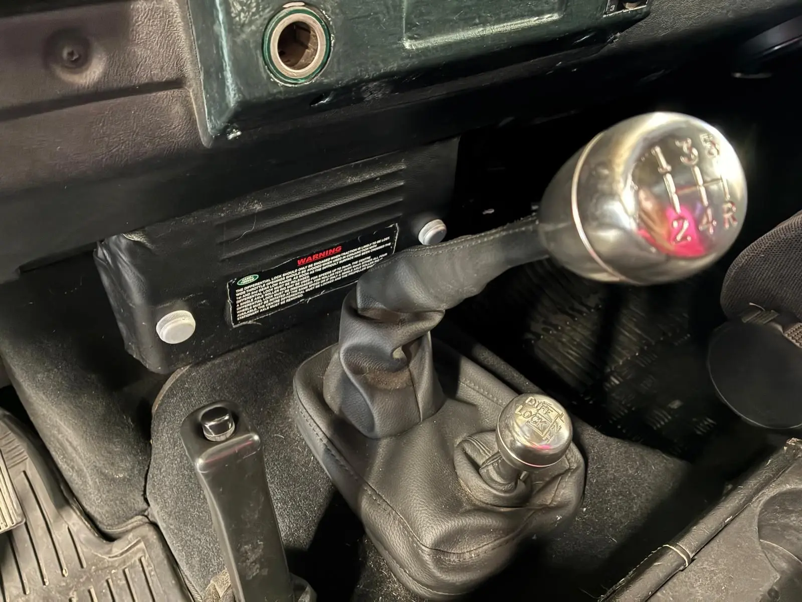 Gros plan intérieur sur le levier de vitesses manuel et le levier de blocage de différentiel du Land Rover Defender 110 vert de 2005.