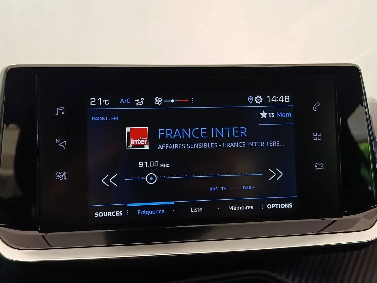 Écran tactile central de la Peugeot 208 blanc, affichant la radio France Inter à 14h48.
