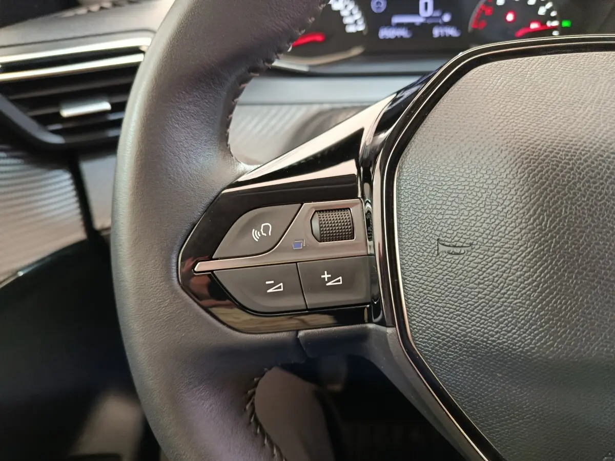 Gros plan sur le volant cuir noir multifonctions côté gauche du Peugeot 208 blanc, avec commandes audio intégrées.
