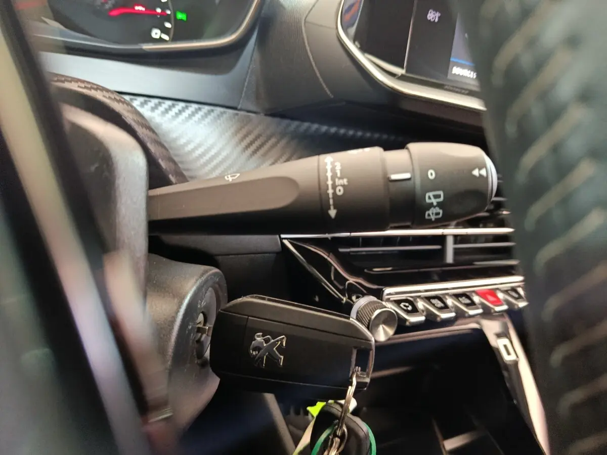 Gros plan sur la clé Peugeot insérée dans le contact, volant cuir et commandes de l’essuie-glace visibles à droite.