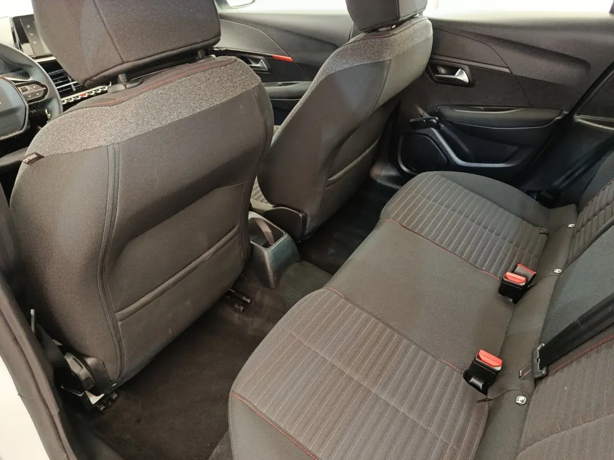 Vue intérieure arrière droite de la Peugeot 208 blanche 2022, sièges tissu gris avec surpiqûres rouges et rangements dos sièges.