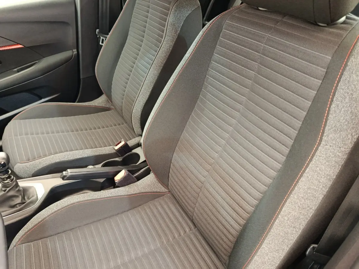Vue rapprochée des sièges avant gris avec surpiqûres rouges et console centrale d'une Peugeot 208 blanche.