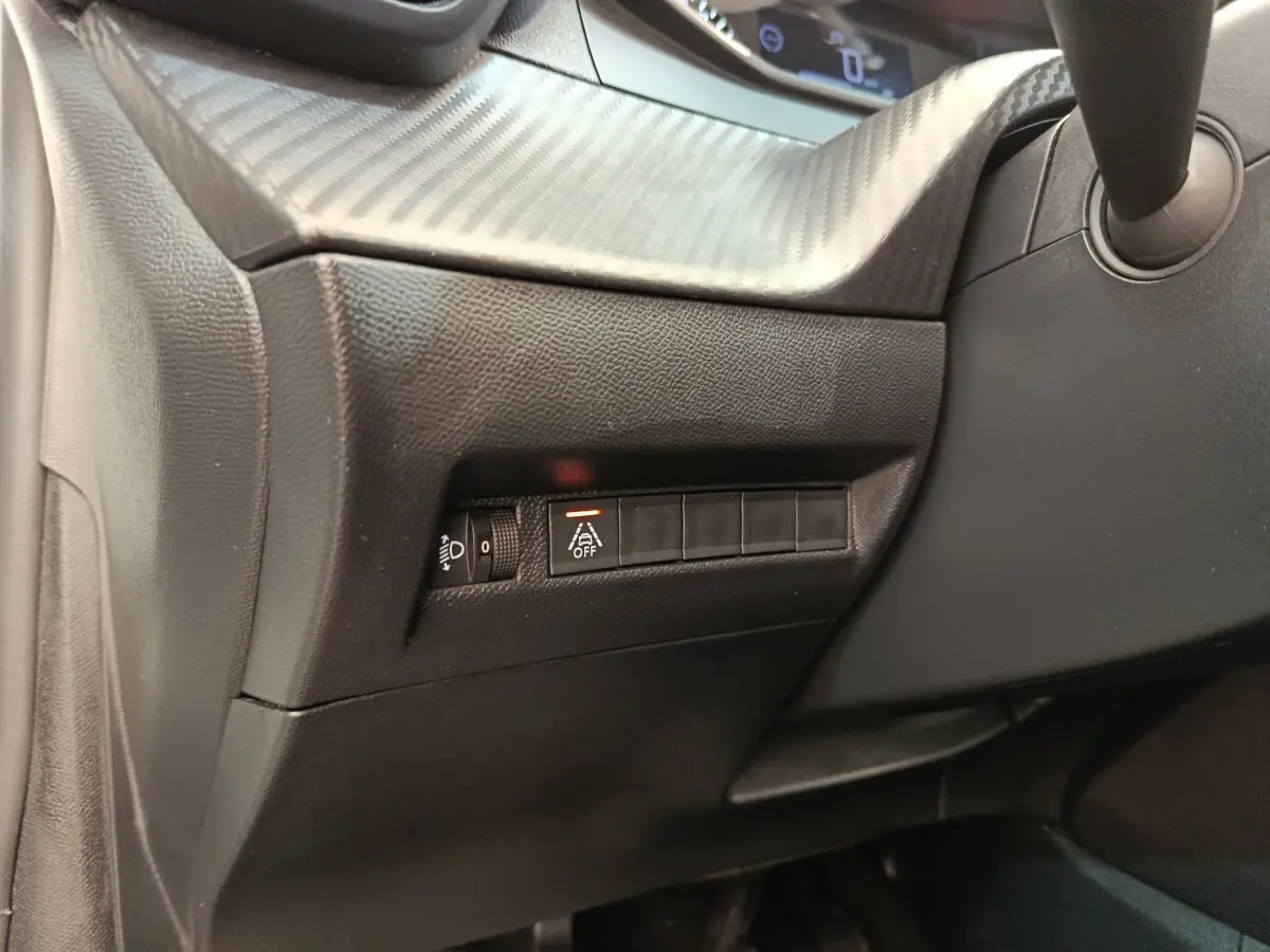 Détail du tableau de bord côté gauche de la Peugeot 208 blanche, avec commande d’éclairage et bouton d’alerte désactivée.