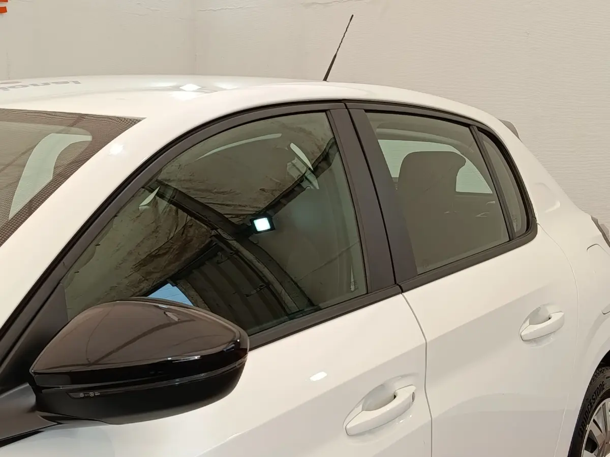 Vue côté gauche arrière d'une Peugeot 208 blanche avec rétroviseur noir brillant et vitres teintées.