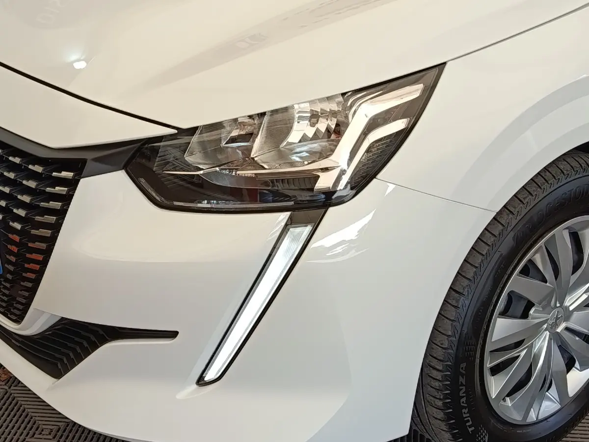 Gros plan sur l'avant droit blanc d'une Peugeot 208 2022, mettant en valeur le phare LED et la roue.