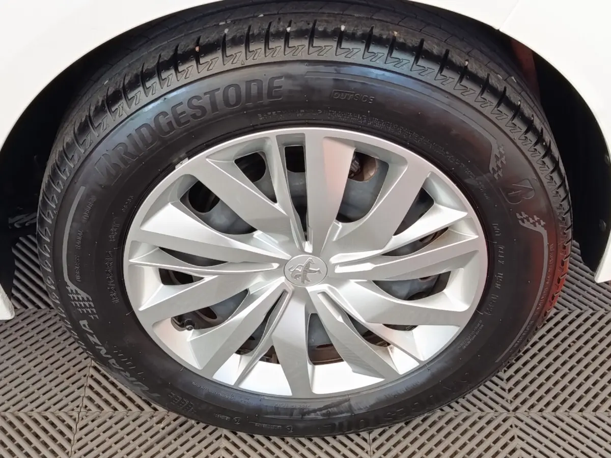 Gros plan sur la roue avant droite d'une Peugeot 208 blanche, mettant en valeur la jante argentée au design moderne.