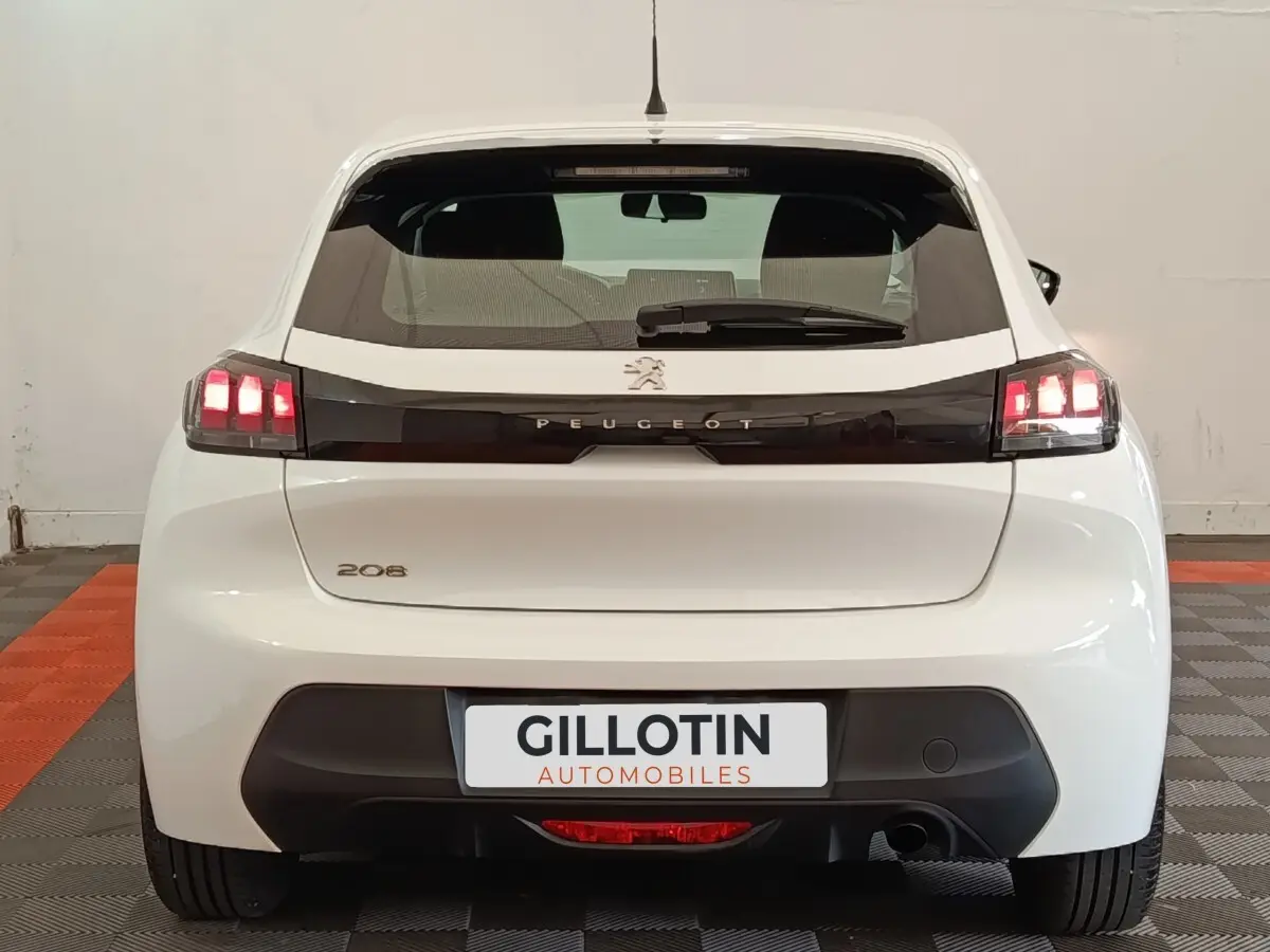 Vue arrière d'une Peugeot 208 blanche 2022 avec feux LED et logo Peugeot sur bande noire brillante.