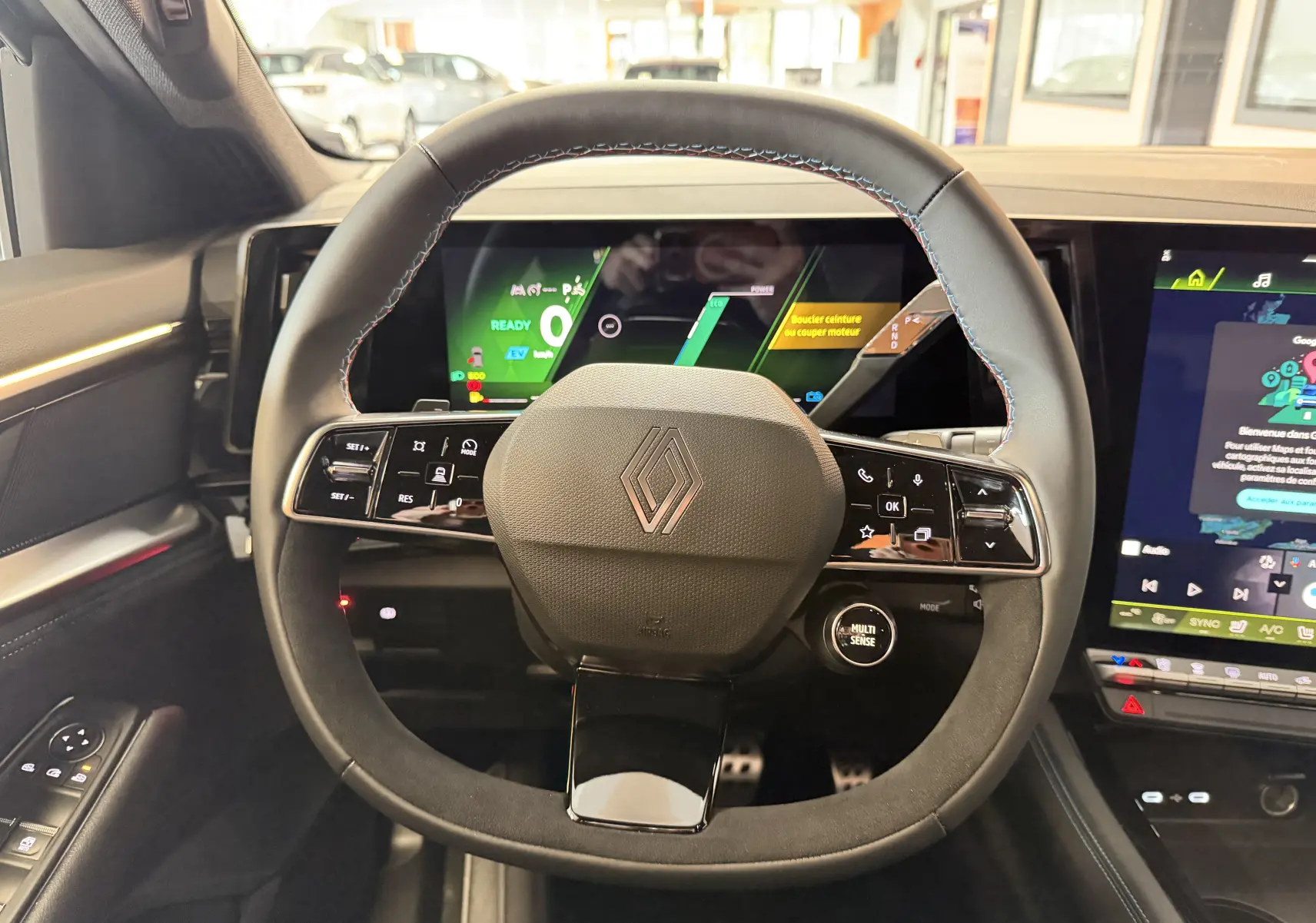 Vue rapprochée du volant multifonction du Renault Austral E-Tech 200 Esprit Alpine avec surpiqûres tricolores et tableau de bord numérique.