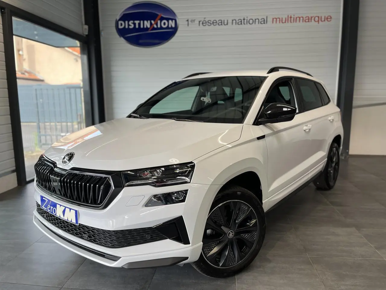 SUV SKODA KAROQ blanc en 3/4 avant droit avec calandre noire et jantes alliage noires dans un showroom.