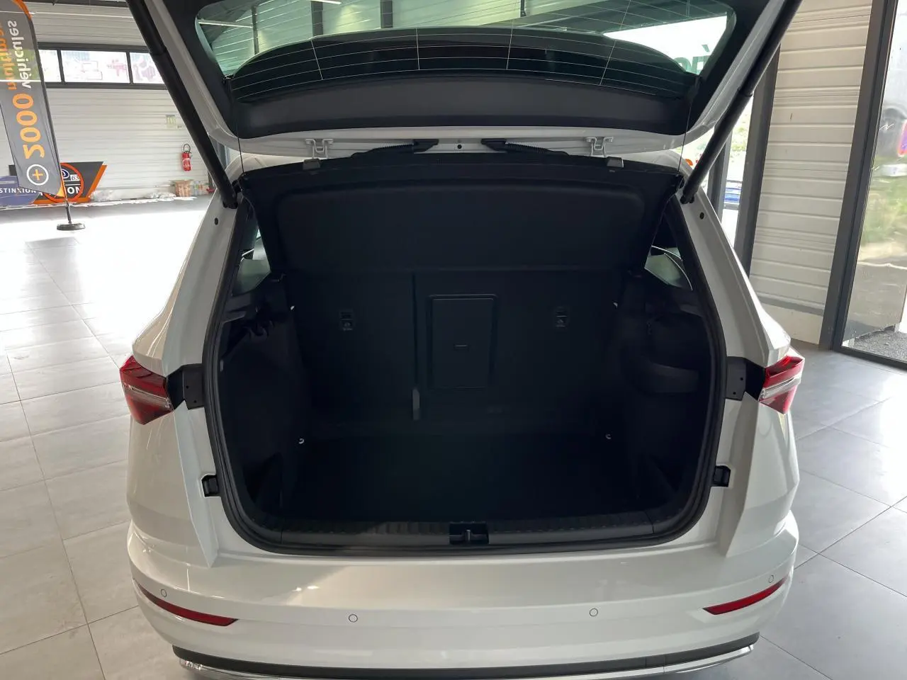 Coffre ouvert vu de l'arrière d'un SUV SKODA KAROQ blanc 2025 avec hayon électrique et feux arrière LED.