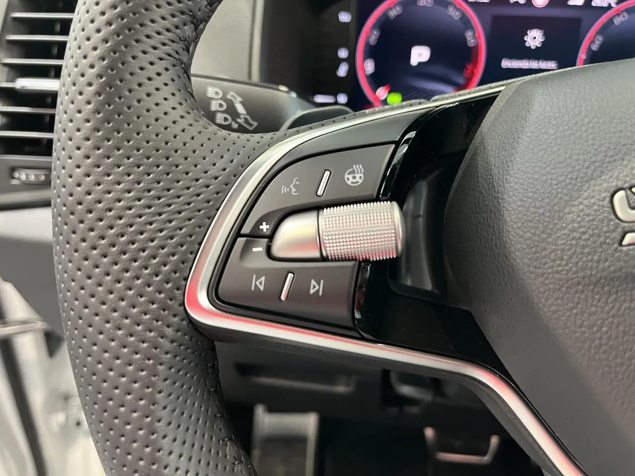 Gros plan sur la partie gauche du volant cuir perforé du Skoda Karoq blanc 2025 avec commandes multifonctions et molette argentée.