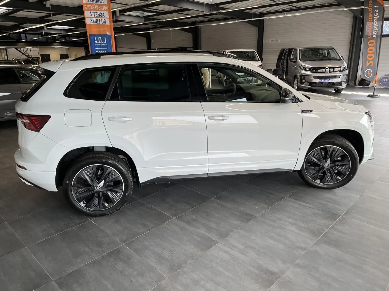 Profil droit du SUV blanc SKODA KAROQ 2025 version Sportline avec jantes alliage noires et détails noirs brillants.