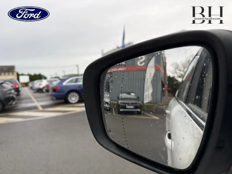 Rétroviseur côté gauche montrant un Renault Espace blanc Glacier garé sous la pluie, vue partielle du véhicule.
