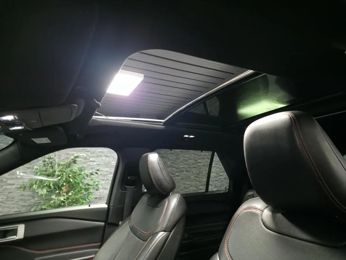 Vue intérieure du Ford Explorer gris, montrant les sièges avant en cuir noir avec surpiqûres rouges et toit panoramique ouvert.