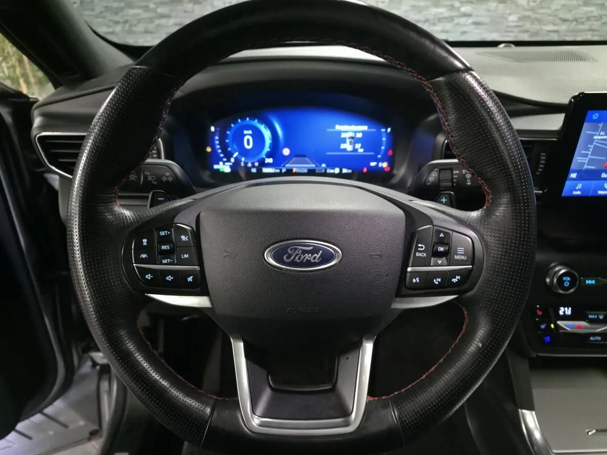 Vue rapprochée du volant noir perforé avec surpiqûres rouges du Ford Explorer 2020, tableau de bord numérique bleu en arrière-plan.