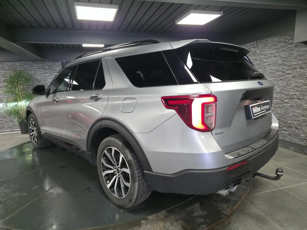Vue 3/4 arrière droit du Ford Explorer gris métallisé avec attelage et jantes alliage noires brillantes en intérieur showroom.