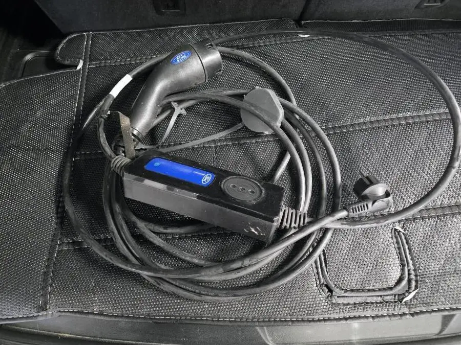 Câble de recharge noir Ford posé sur un tapis de coffre noir, accessoire du Ford Explorer hybride rechargeable gris.