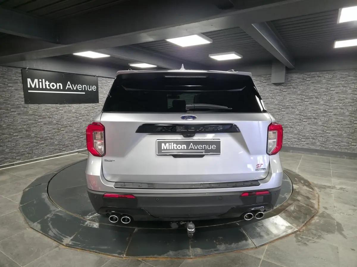 Vue arrière d'un Ford Explorer gris métallisé avec quatre sorties d'échappement chromées et attelage visible en intérieur showroom.