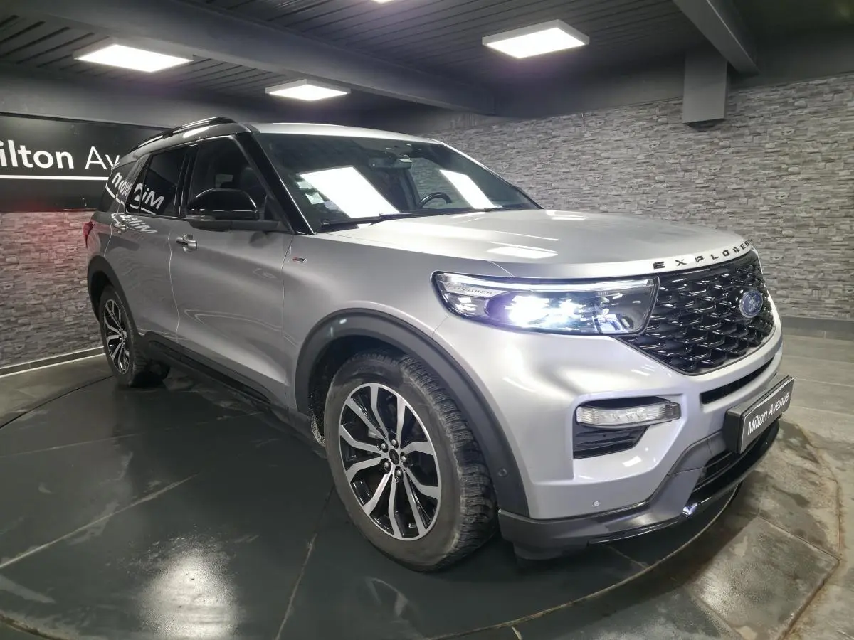 Ford Explorer gris métallisé en vue 3/4 avant droit, avec calandre noire brillante et jantes alliage 20 pouces.