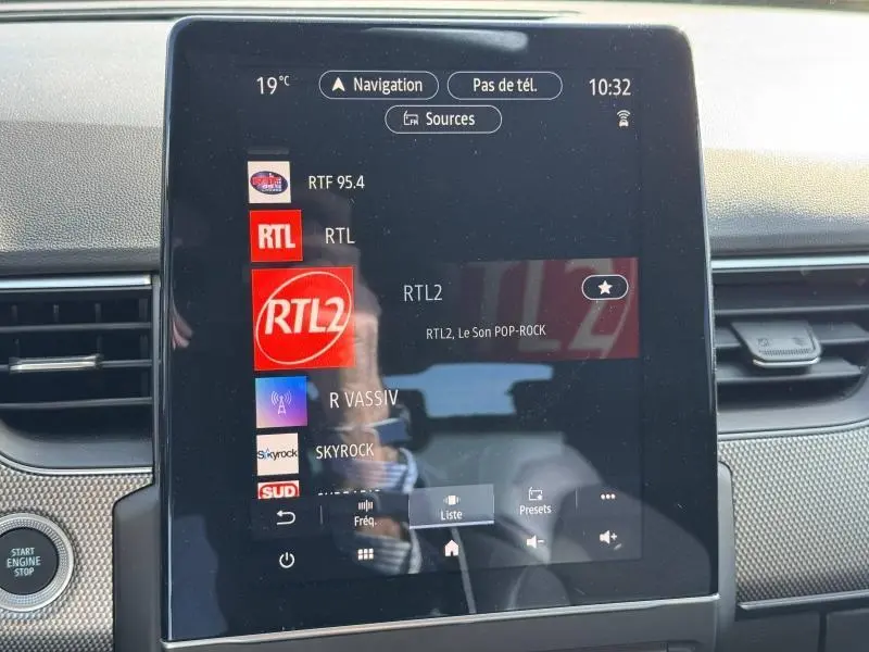 Écran tactile central de la Renault Arkana noir métal 2023 affichant les stations radio avec tableau de bord gris.
