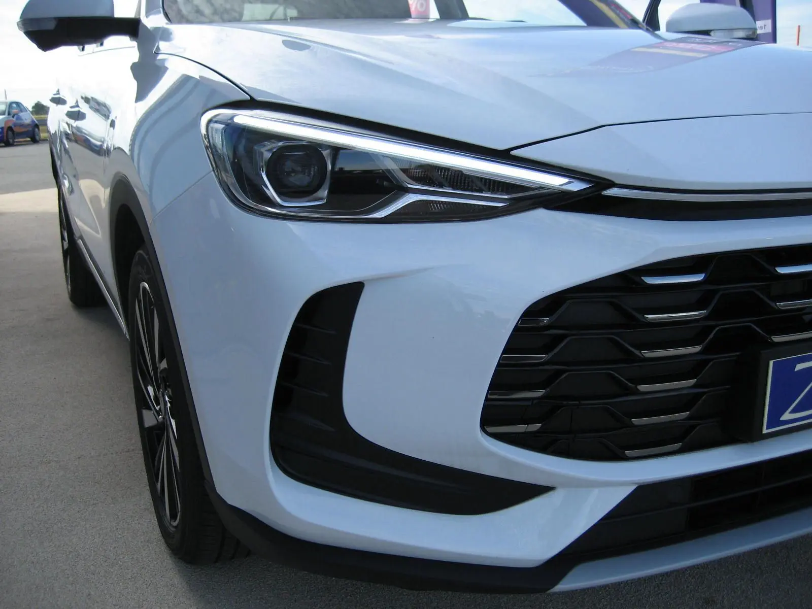 Vue 3/4 avant gauche du MG ZS blanc, mettant en valeur le phare LED et la calandre noire distinctive.