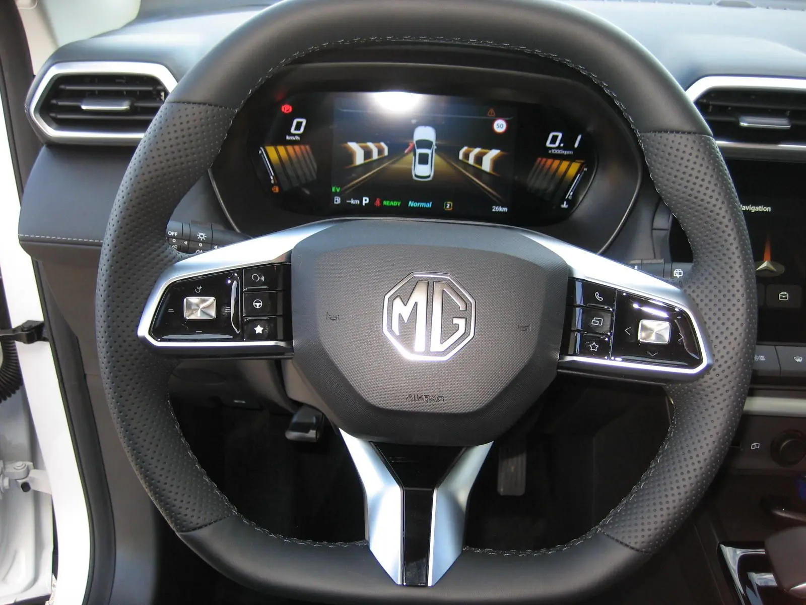 Vue rapprochée du volant noir perforé avec logo MG et tableau de bord numérique du MG ZS 1.5 HYBRID+197 LUXURY blanc 2026.