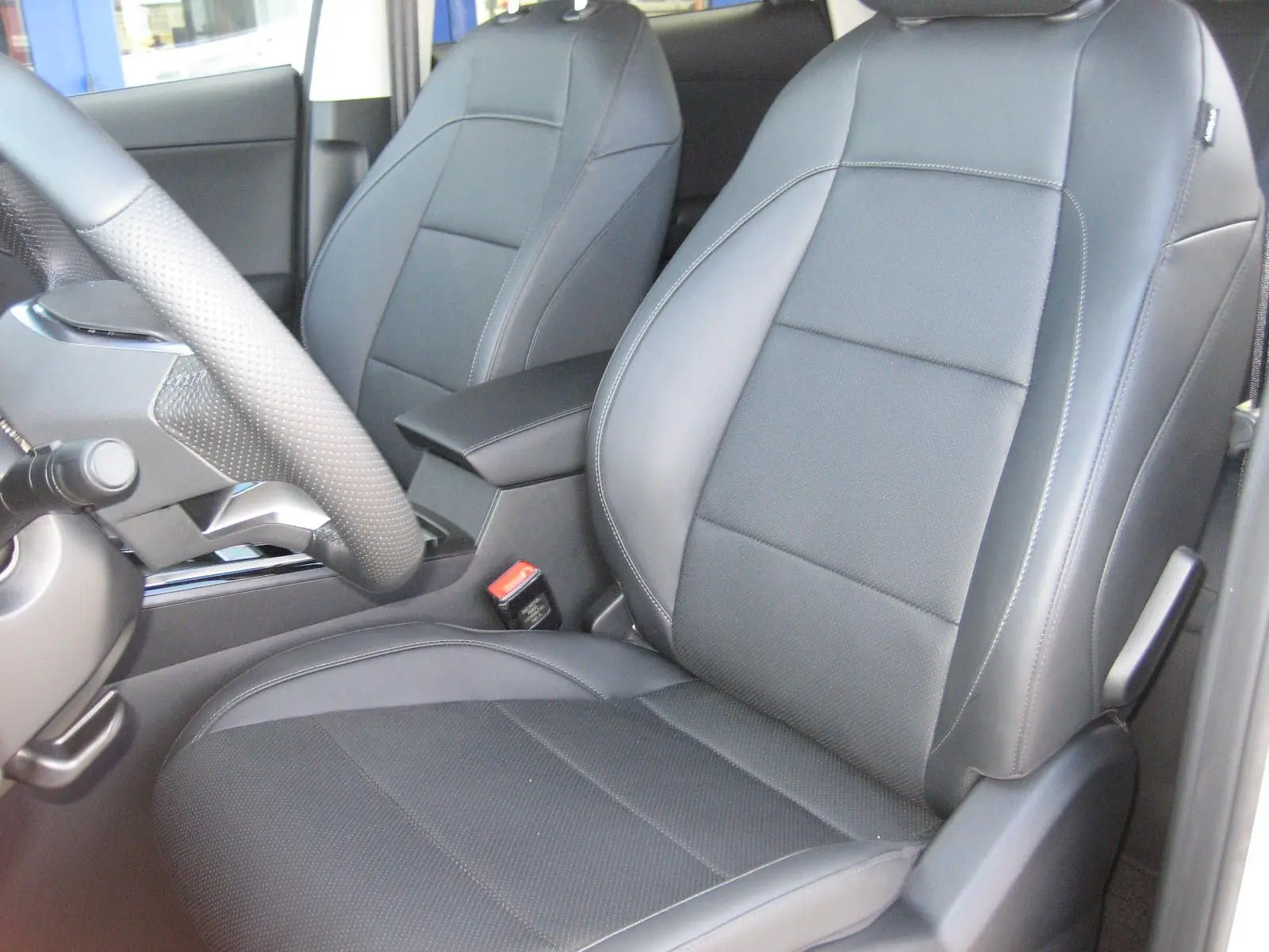 Gros plan sur les sièges avant en cuir noir du MG ZS 1.5 HYBRID+197 LUXURY blanc, avec accoudoir central visible.