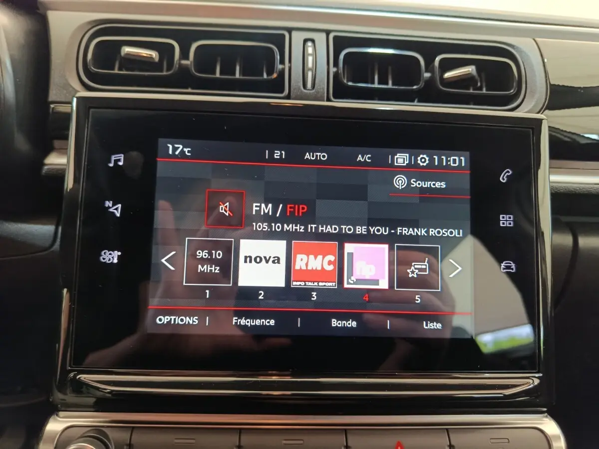 Gros plan sur l'écran tactile central du tableau de bord de la Citroën C3 blanche, affichant la radio FM avec plusieurs stations.