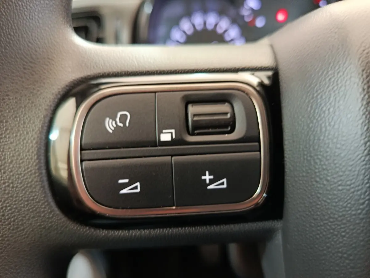 Gros plan sur les commandes multifonctions noires du volant de la Citroën C3 blanche, avec boutons de volume et gestion d'appels.