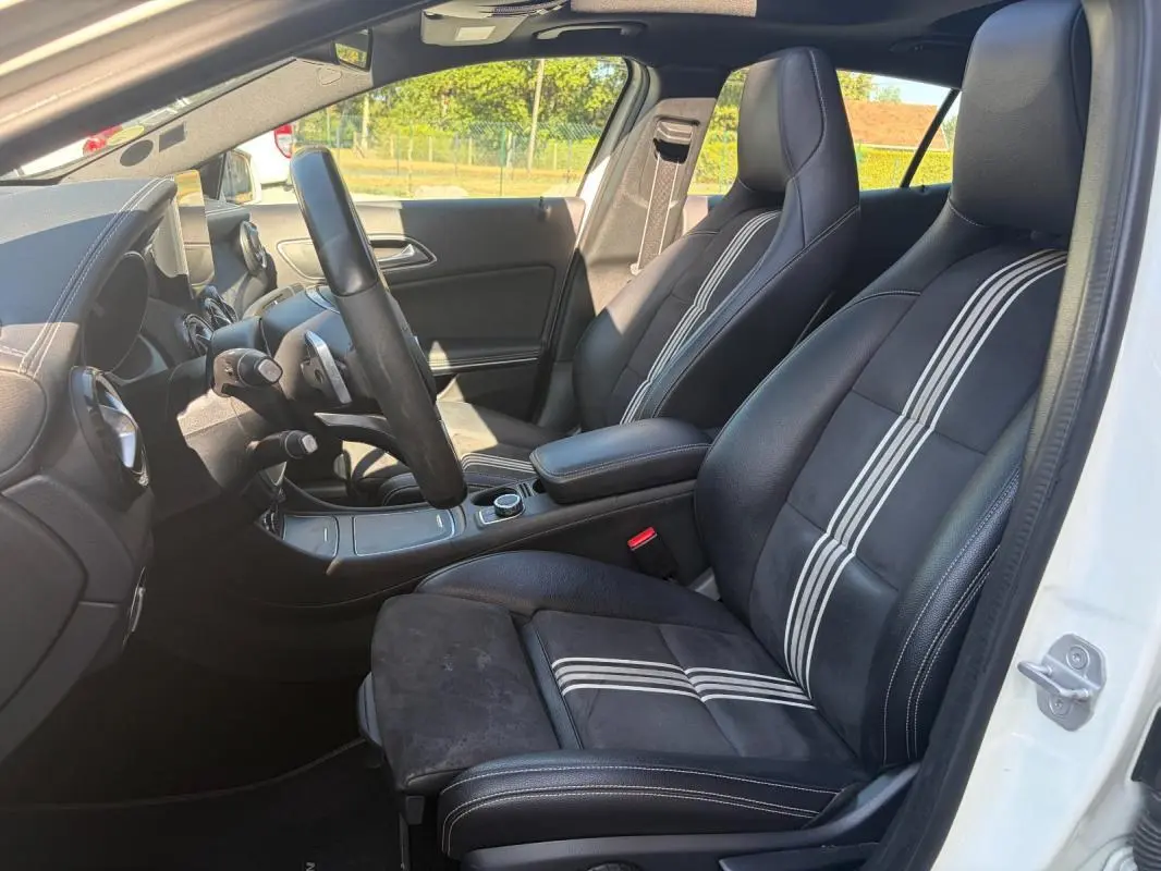 Vue intérieure côté conducteur du Mercedes GLA 220d blanc, mettant en valeur les sièges noirs avec bandes blanches et le tableau de bord.