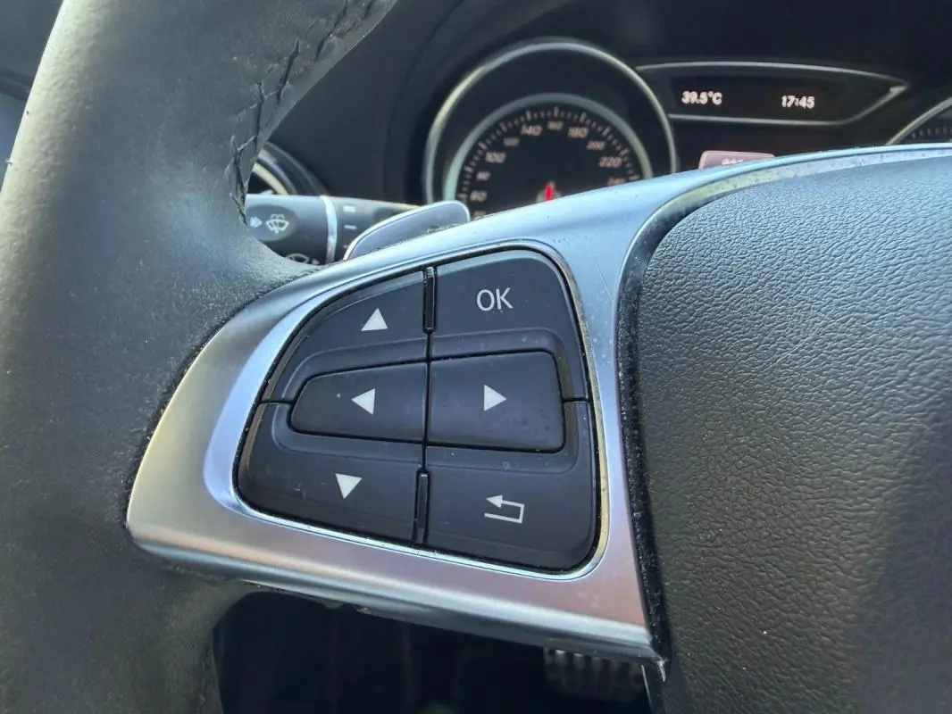 Gros plan sur les commandes au volant côté gauche du Mercedes GLA 220d blanc, tableau de bord en arrière-plan.