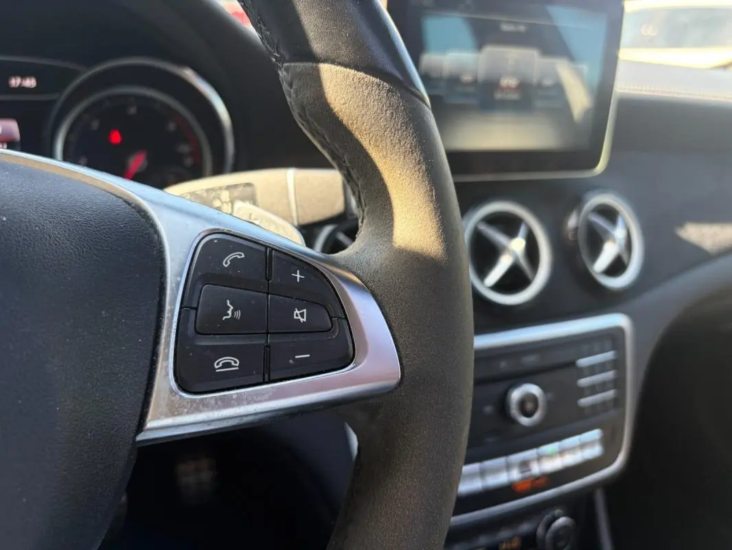 Gros plan sur le volant côté gauche du Mercedes GLA blanc 2017, avec commandes audio et aérateurs ronds en arrière-plan.