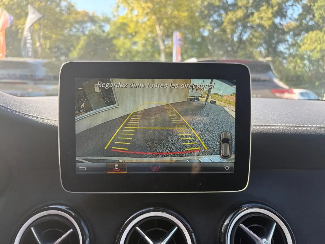 Écran central montrant la caméra de recul avec lignes de guidage dans un Mercedes GLA blanc, vue intérieure avant.