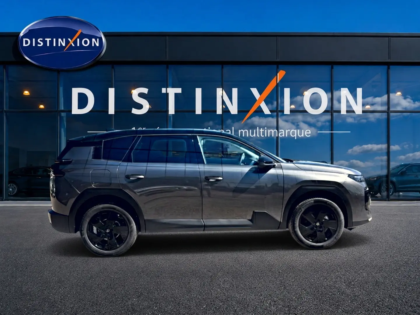 Profil droit du Citroën C5 Aircross gris platinium avec toit noir et jantes alliage noires devant une vitrine Distinxion.