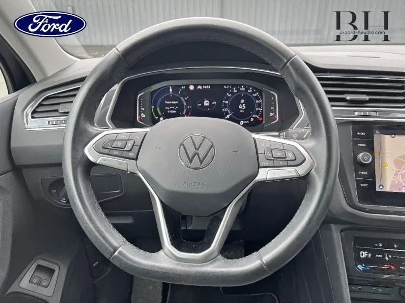 Vue intérieure centrée sur le volant cuir multifonction d'un Volkswagen Tiguan noir avec tableau de bord numérique et écran tactile.