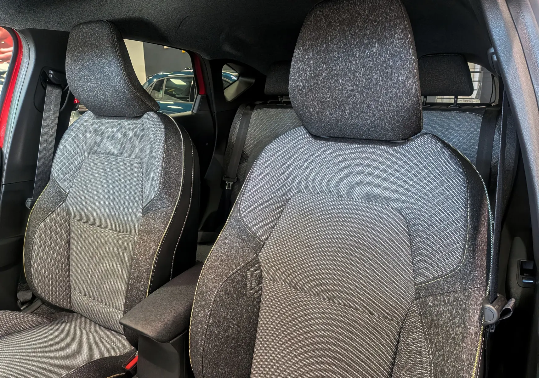 Gros plan sur les sièges avant en tissu gris du Renault Captur E-TECH 2025, avec portières rouges visibles en arrière-plan.