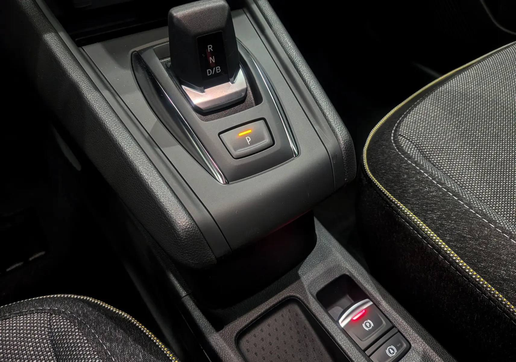 Gros plan sur la console centrale du Renault Captur hybride 2025, avec levier de vitesses automatique et sièges tissu noirs.