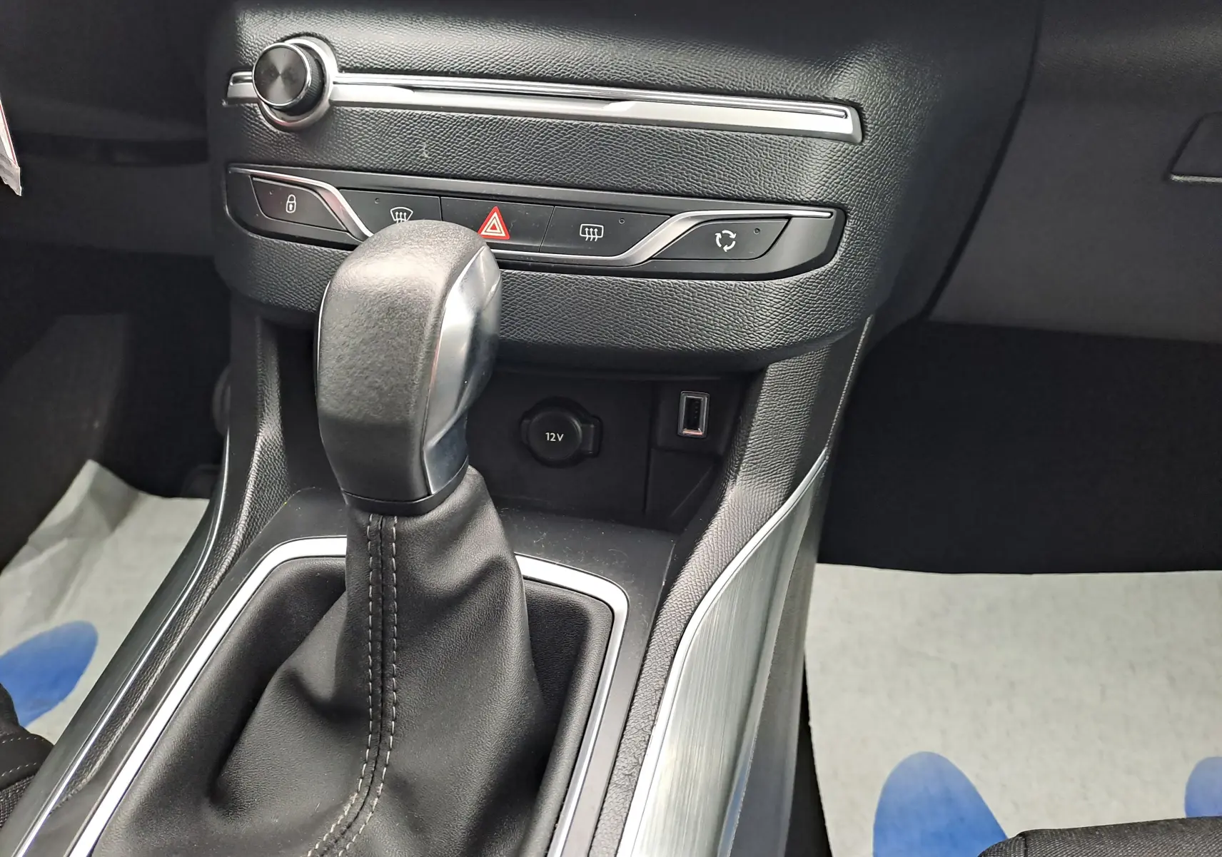 Gros plan sur la commande de boîte automatique en cuir noir et plastique argenté dans une Peugeot 308 gris 2019.