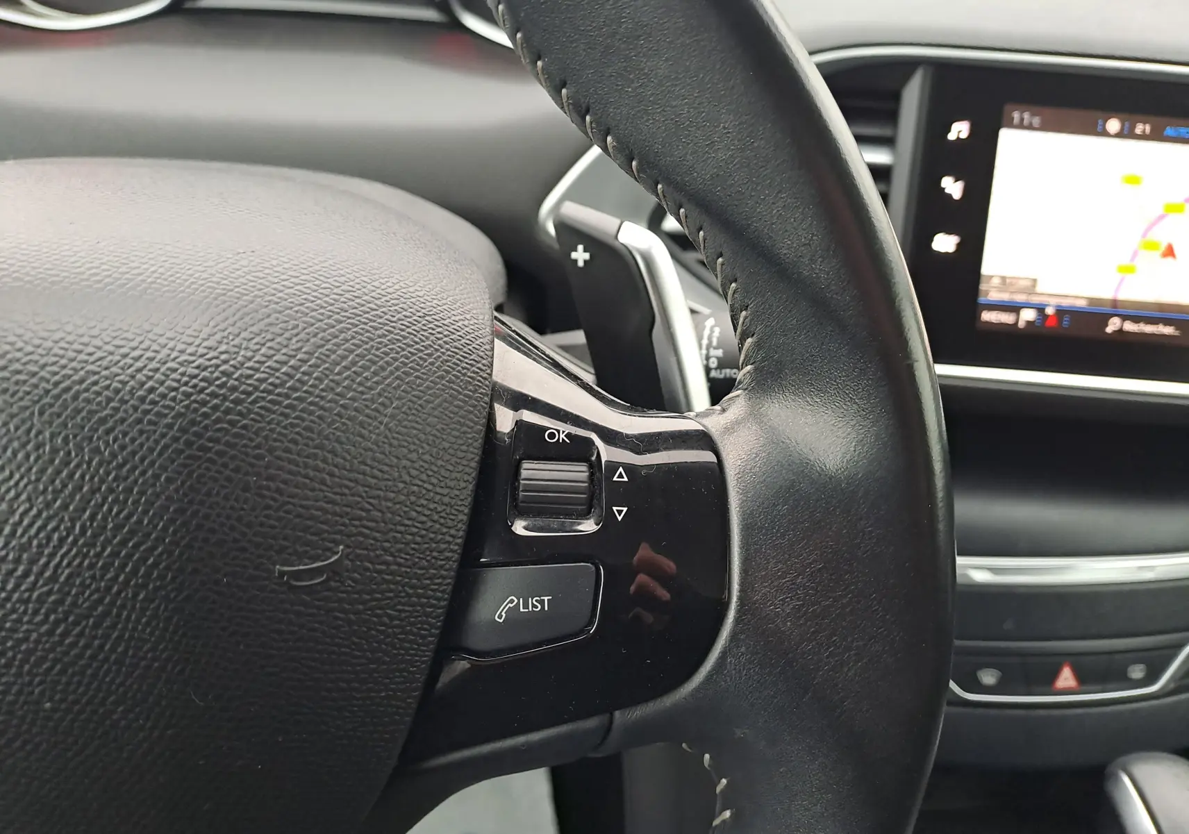 Gros plan sur le volant en cuir noir de la Peugeot 308 2019 avec commandes intégrées et écran tactile du tableau de bord.