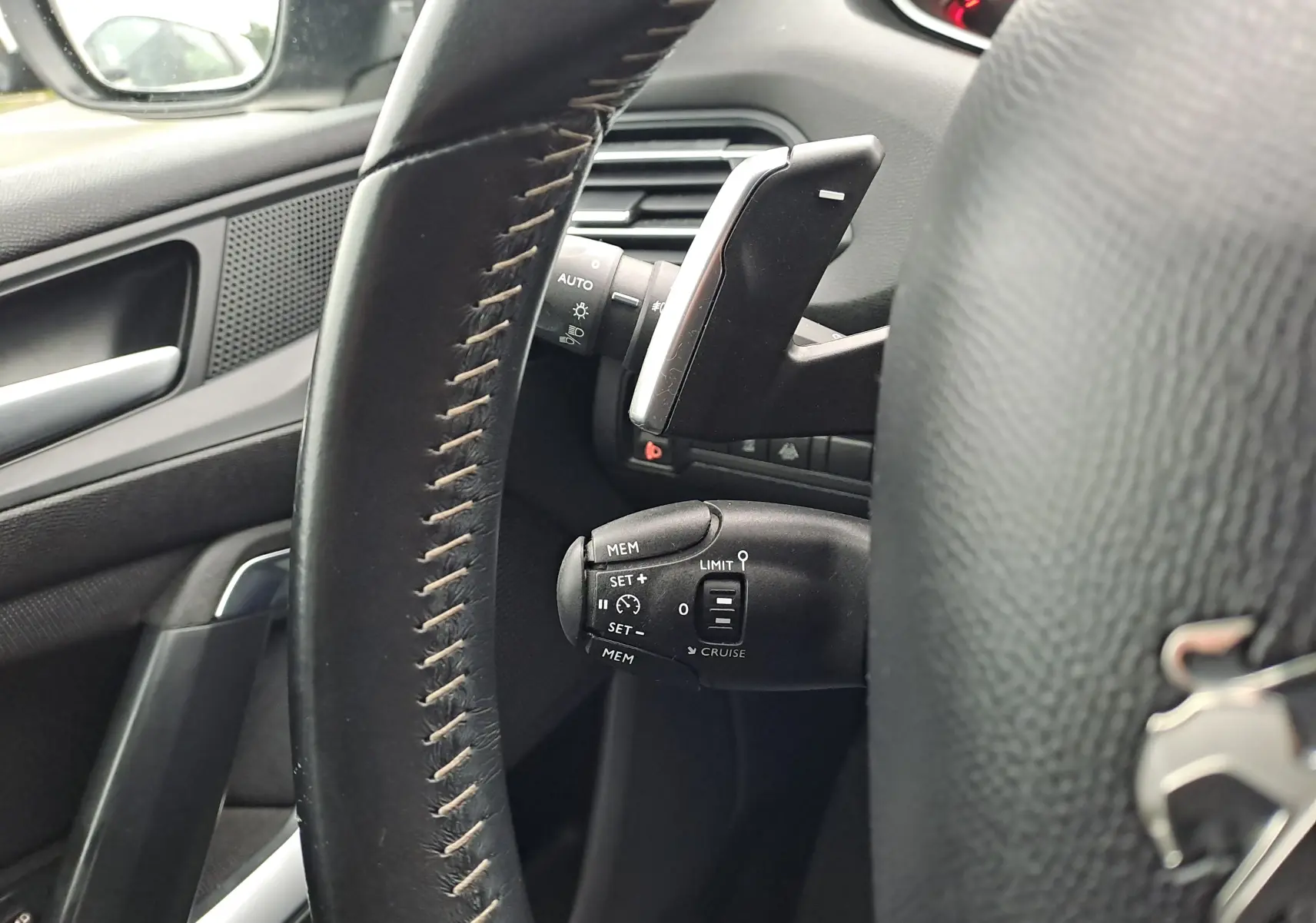 Gros plan sur le volant en cuir noir et les commandes de régulateur de vitesse côté gauche d'une Peugeot 308 gris 2019.