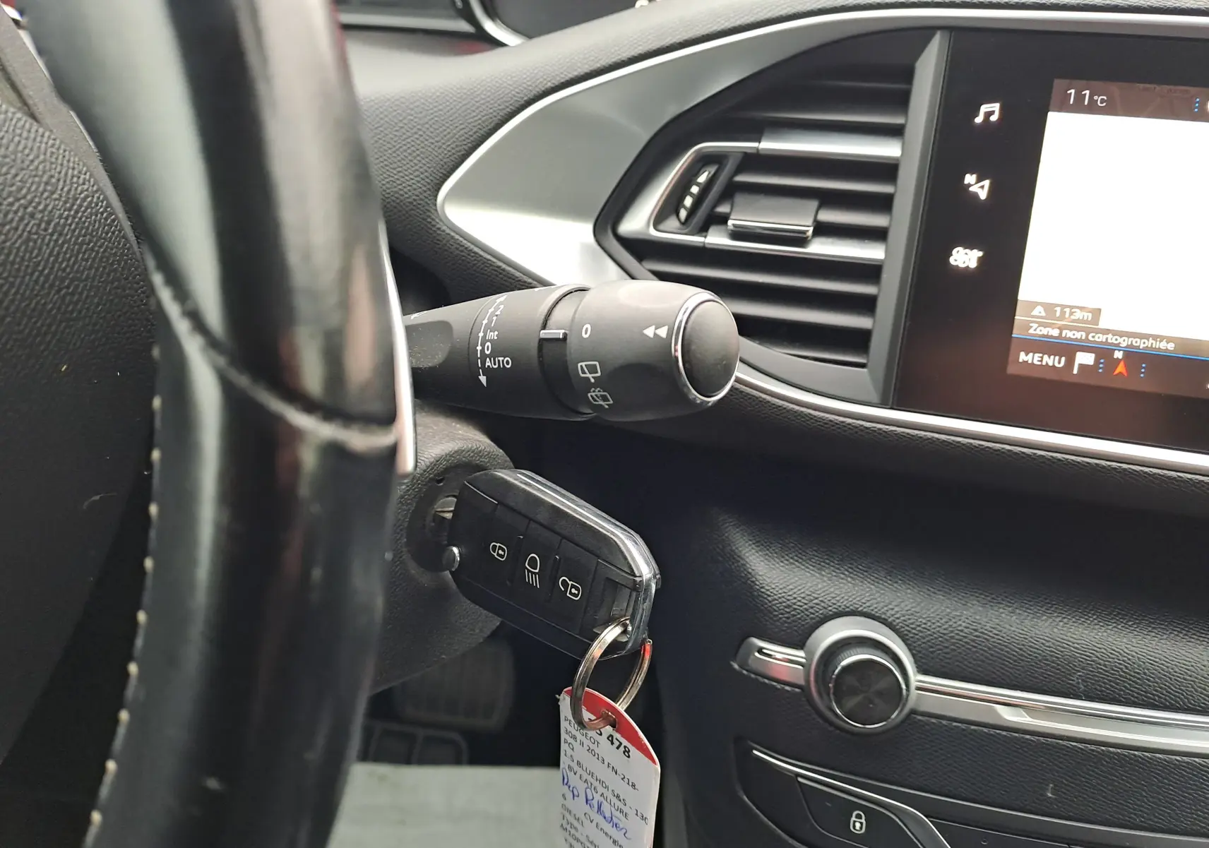 Gros plan sur le volant et la clé insérée du Peugeot 308 gris, avec l'écran tactile et la commande d'essuie-glace visibles.