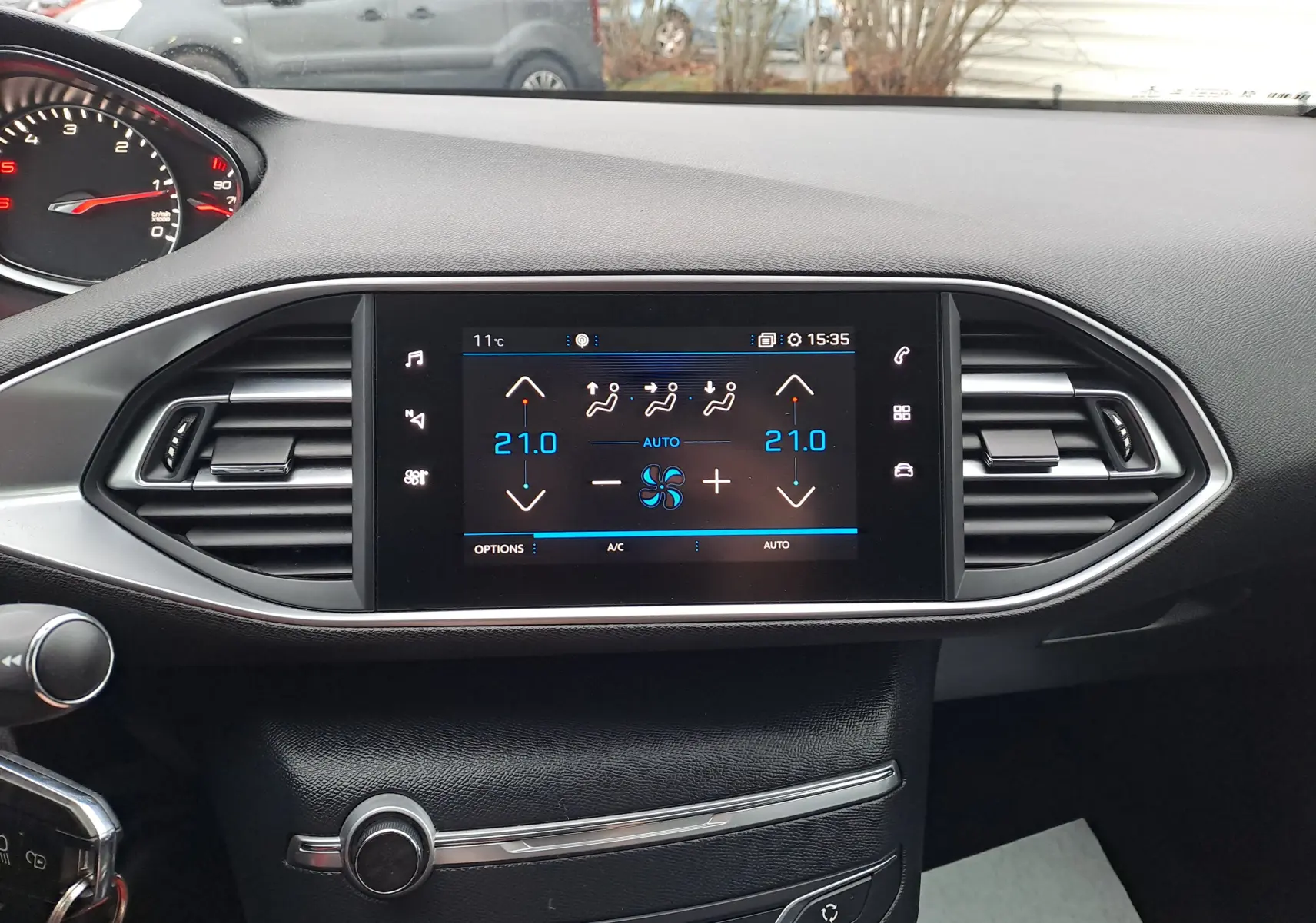 Tableau de bord intérieur de Peugeot 308 gris, vue frontale sur l'écran tactile de climatisation digitale à 21°C.