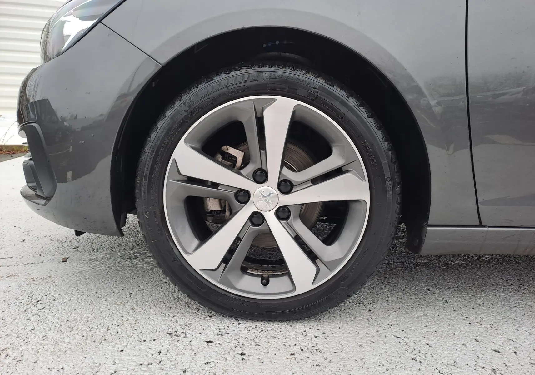 Gros plan sur la roue avant gauche grise d'une Peugeot 308 2019 avec jante alliage à cinq branches.